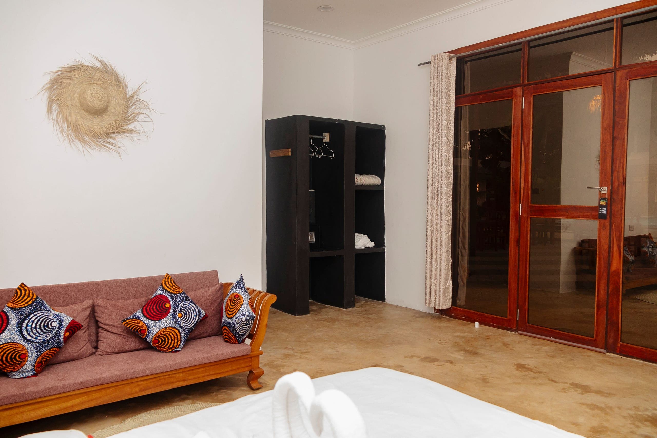 Daybed with kanga cushions beside an open wardrobe and glass doors onto the terrace