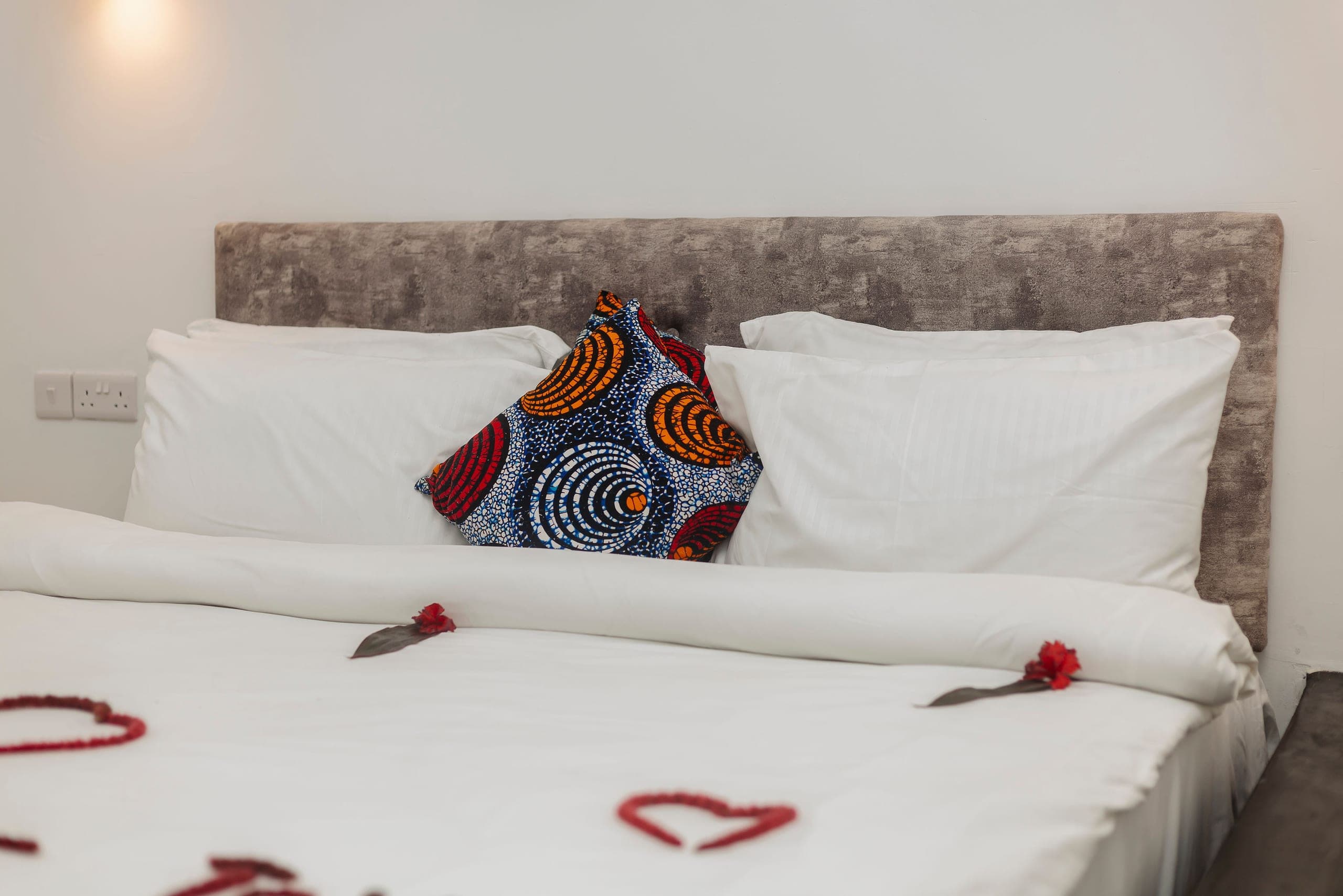 Crisp white pillows with a printed kanga cushion against a soft grey headboard