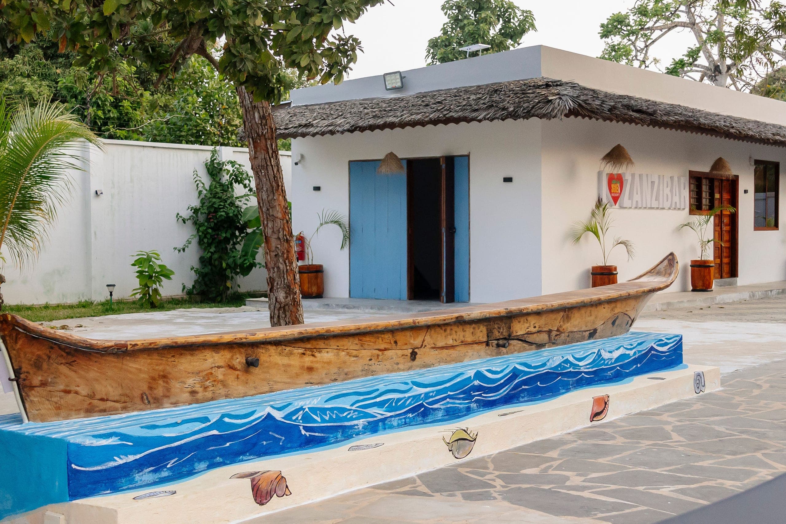 A carved wooden dhow resting on a painted wave mural in the courtyard