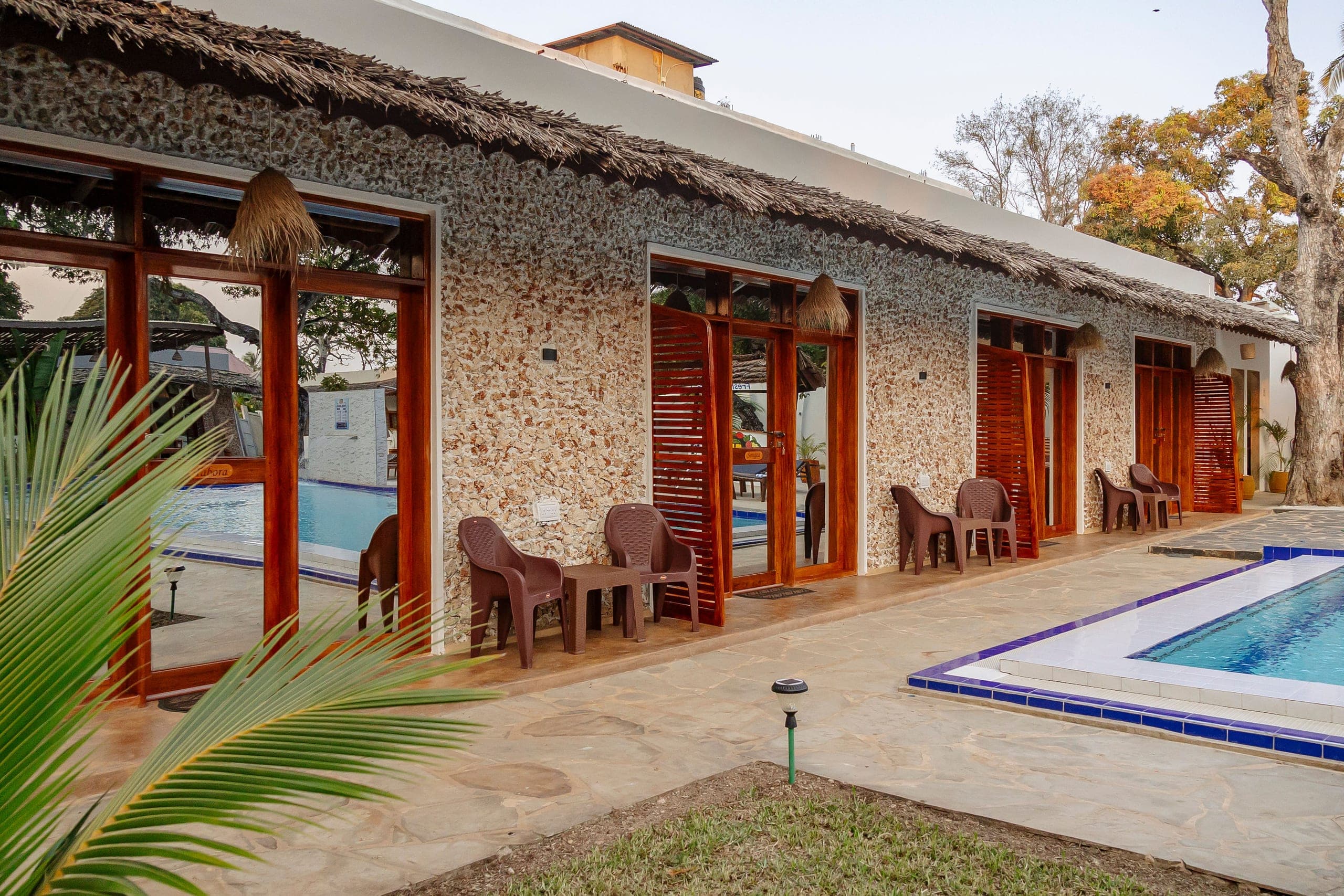 Coral stone room fronts with red shutters opening onto the pool terrace
