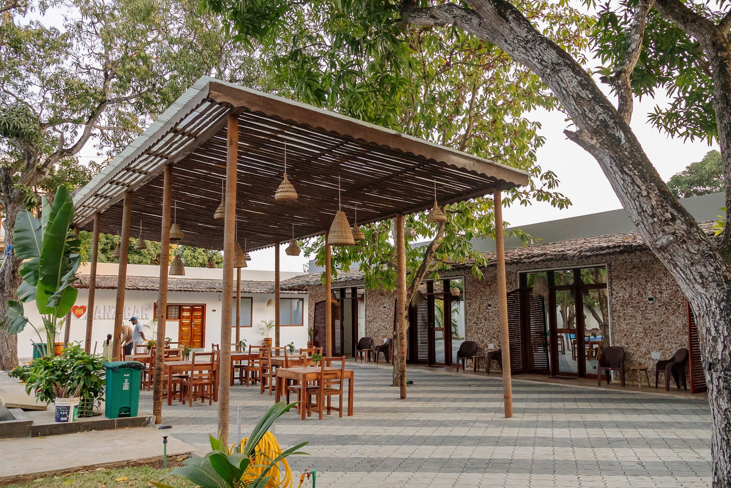 Wooden tables under the restaurant pergola, shaded by mango trees