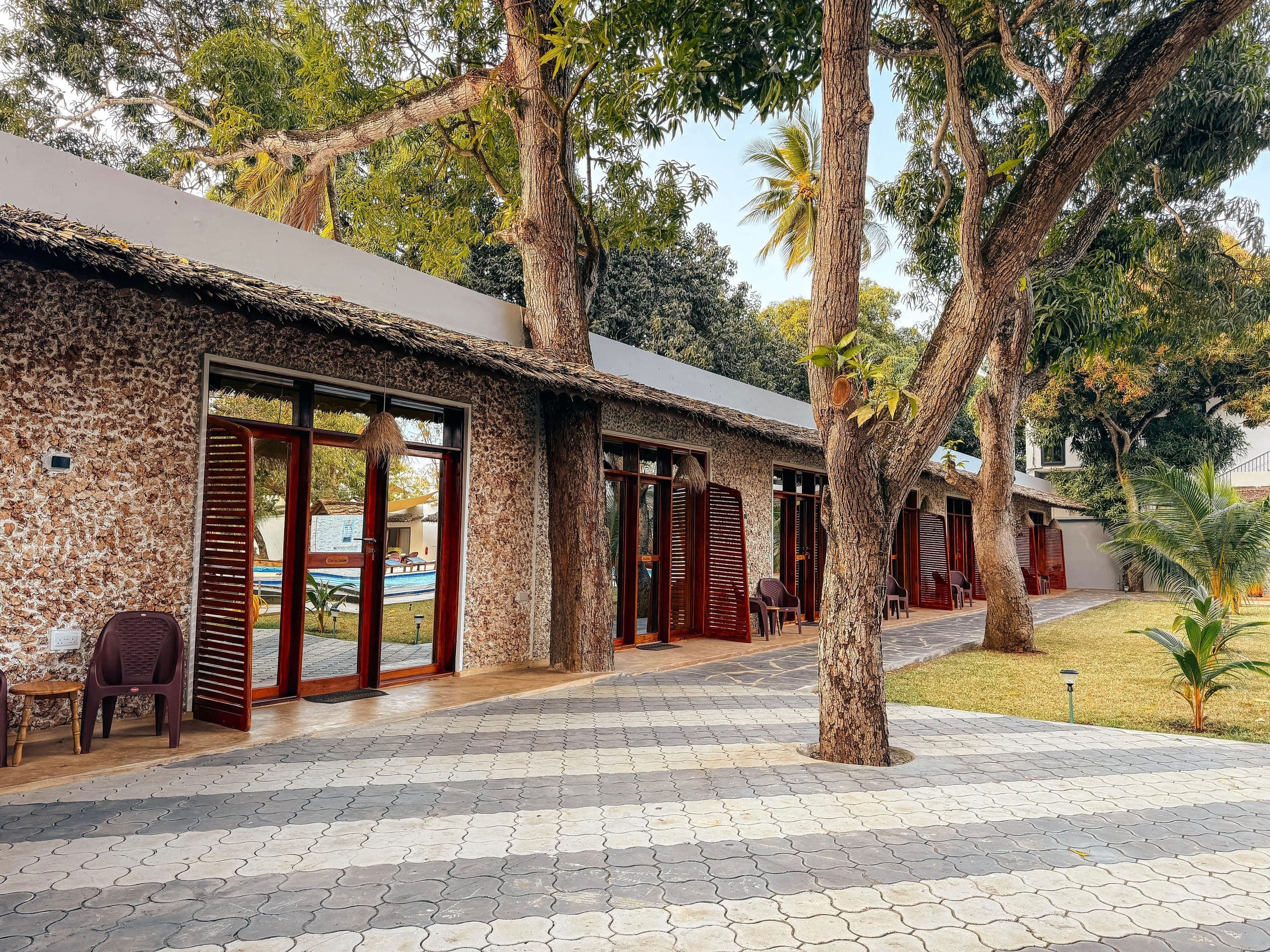 Coral stone room fronts with red shutters, shaded by old mango trees