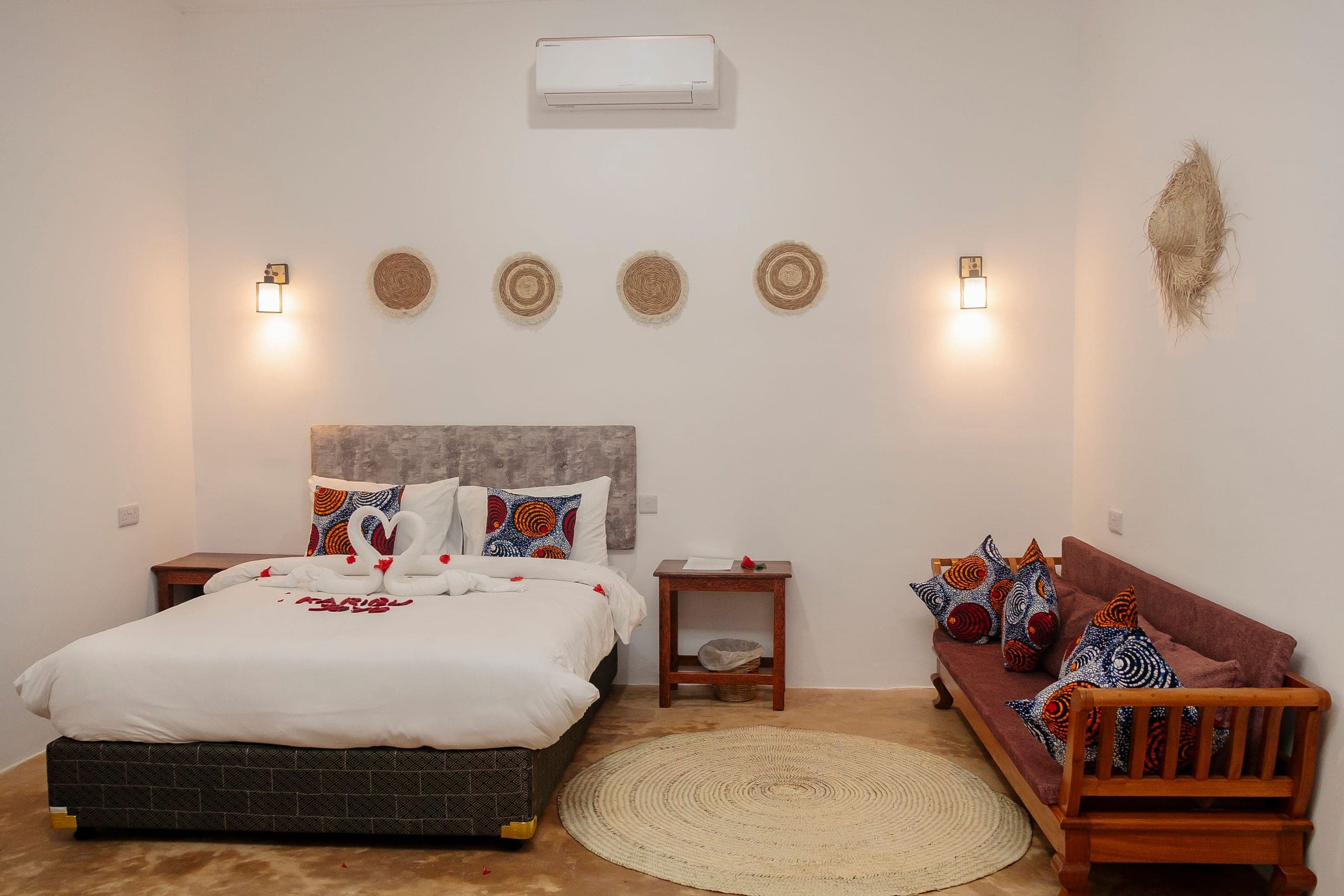 Deluxe room with a wide bed dressed in white linen, a kanga-cushioned daybed and woven wall discs