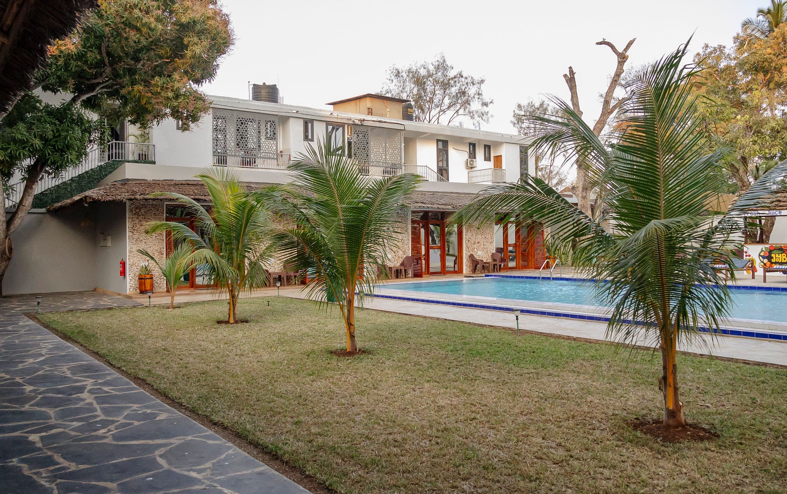 The lawn at JoyB Resort, young palms running down to the poolside under old mango trees