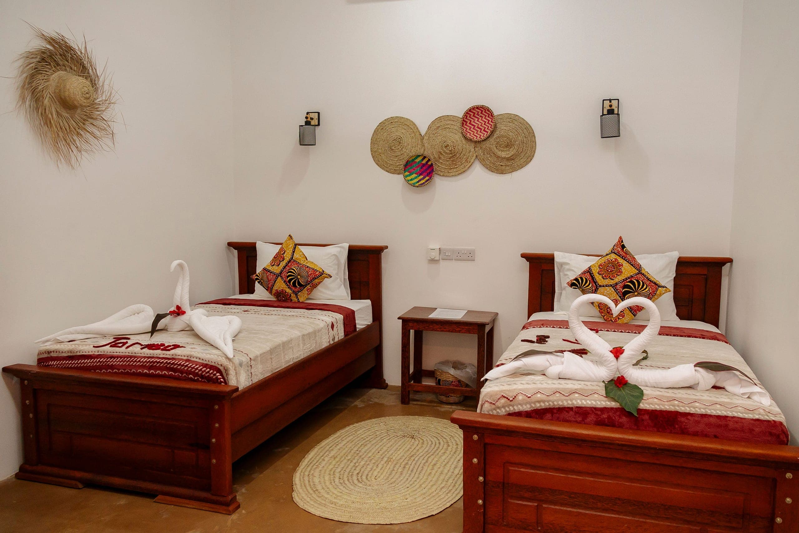 Twin room with two carved wooden beds, kanga cushions and woven baskets on the wall